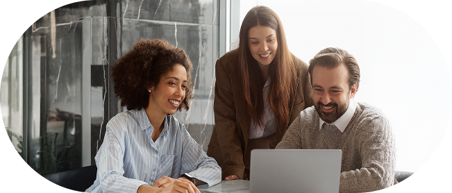 A group of three people consisting of two women and one man, all three looking at a notebook while smiling, and they are all wearing business attire (sweaters, dress shirts, etc.).